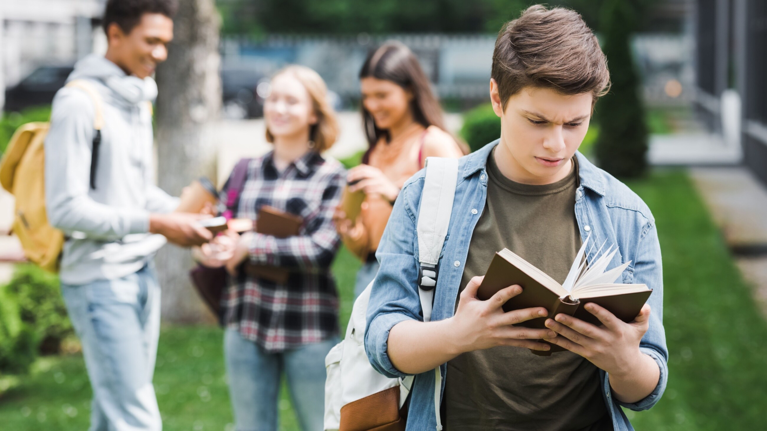 Selective focus of teenager reading book with friends on background.