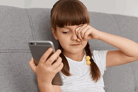 girl on mobile phone rubbing her eyes from too much screen time