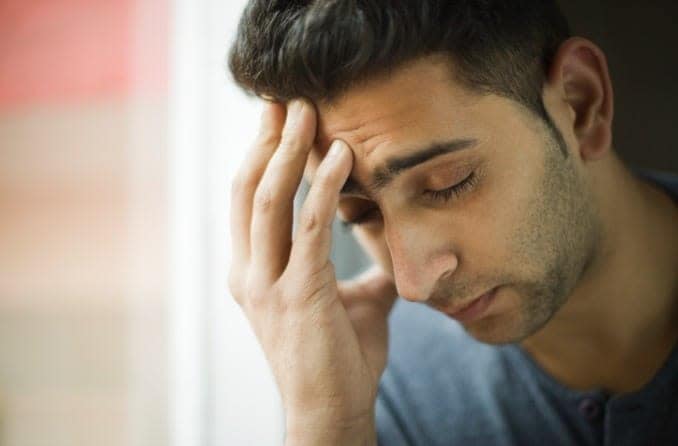 Headache causes a dark-haired young man to close his eyes and massage his forehead. Headache causes a dark-haired young man to close his eyes and massage his forehead.