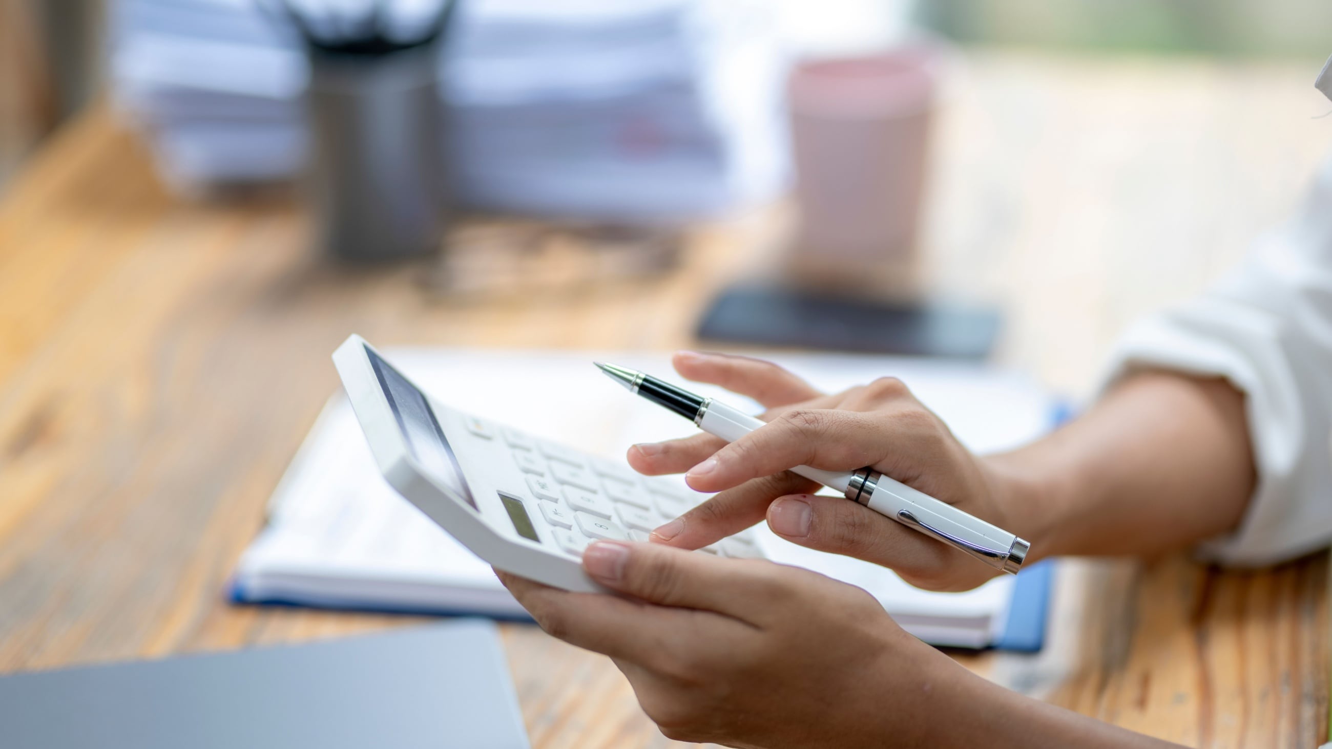 A woman is using a calculator and pen on a desk.