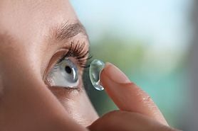 Young woman putting contact lens in her eye.