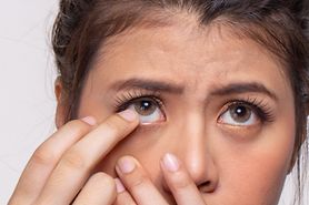 A woman with one finger near her eye as she struggles to remove a stuck contact lens.