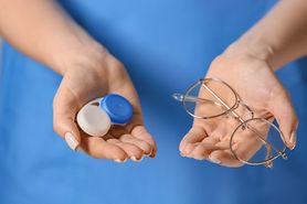 An optician holding contact lenses in a contact lens case in one hand and glasses in her other hand. An optician holding contact lenses in a contact lens case in one hand and glasses in her other hand.