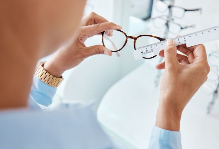 An optician measuring the frame size of a pair of glasses with a ruler at the eye doctor.