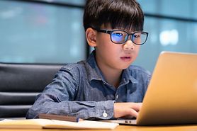 young boy wearing blue light blocking glasses looking at laptop screen