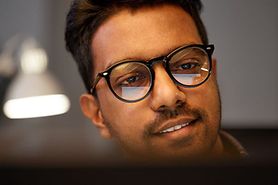 man wearing eyeglasses with computer screen in reflection of eyeglass lenses
