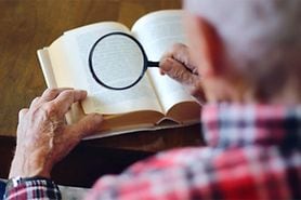 elderly man using low vision magnifier to read a book