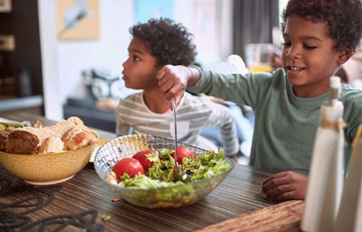boy sitting at kitchen table serving salad